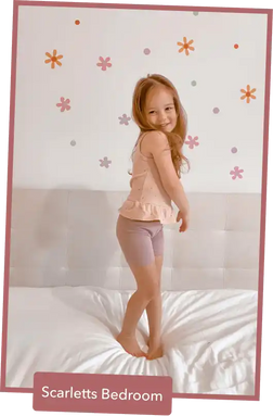 A child in pink sleepwear standing on a bed.